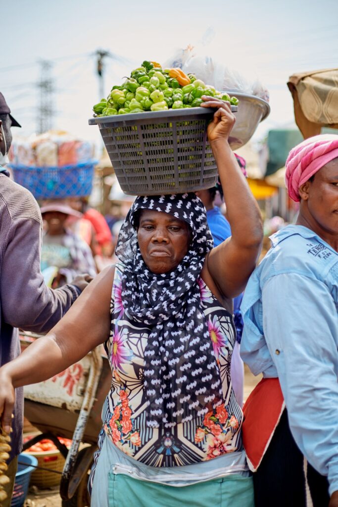 Marktstand mit Frau, die einen Korb Gemüse auf dem Kopf trägt, in Accra, Ghana